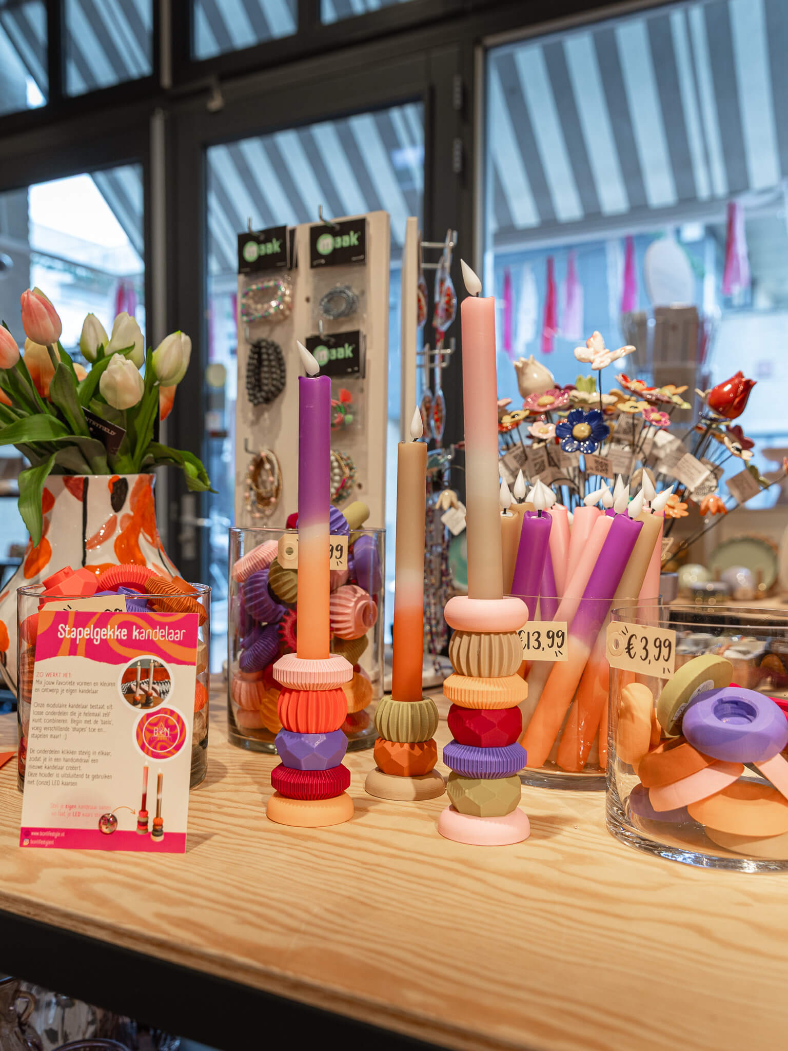 Een winkelpresentatie met kleurrijke kaarsen, kandelaars, bloemen en cadeauartikelen in de winkel van Makers en Merken.