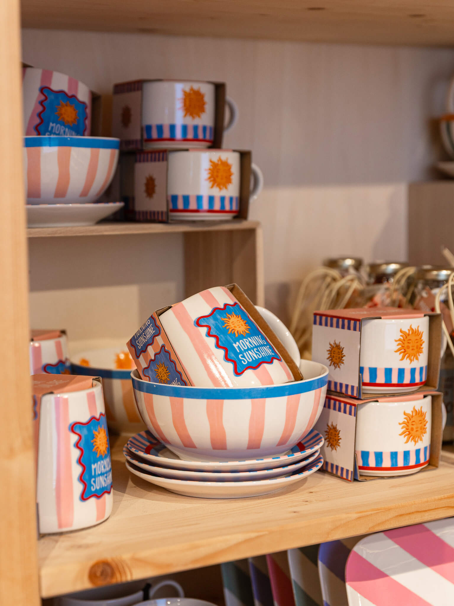Gekleurde mokken, kommen en borden staan uitgestald op een houten schap in de winkel van Makers en Merken.