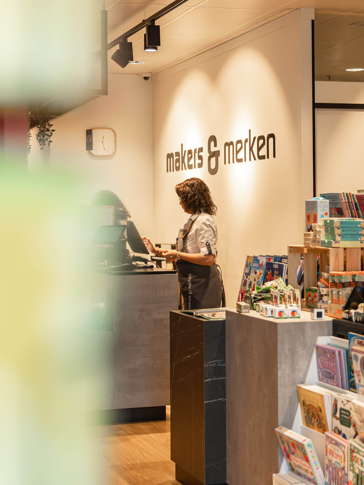 Cadeauwinkel Makers & Merken Nijmegen in het Radboud ziekenhuis Een medewerker staat achter de balie van Makers & Merken Nijmegen in het Radboud ziekenhuis, tussen boeken, cadeaus en unieke producten van de makers.
